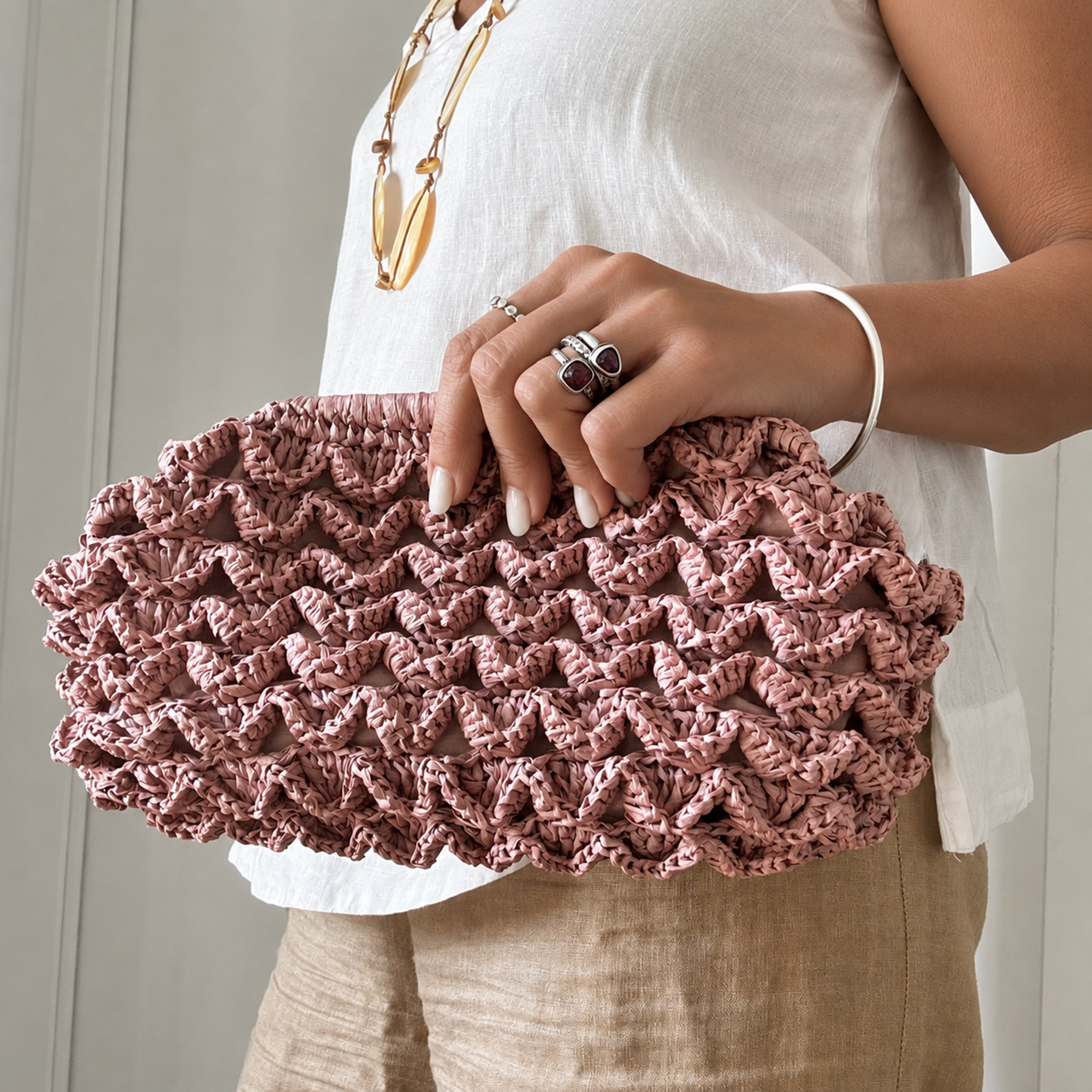 Duna, clutch artigianale in rafia rosa lavorata all'uncinetto, indossata a mano.