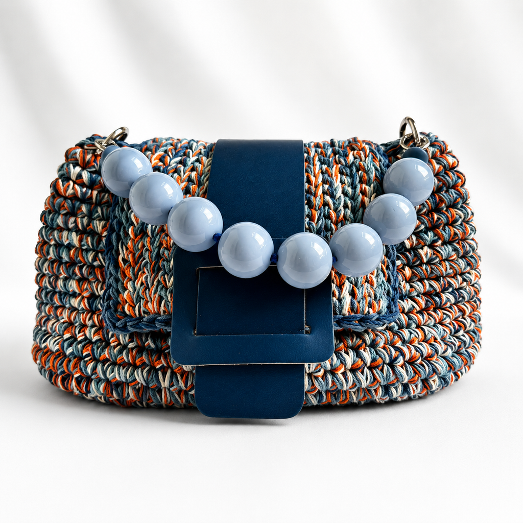 Vista frontale della borsa crochet Kia blu con chiusura e manico di perle.