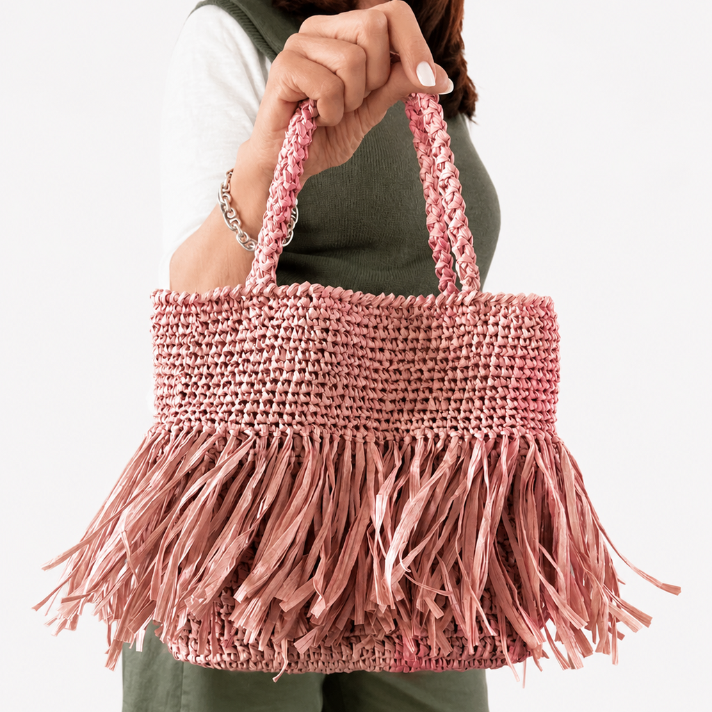 Borsa artigianale in rafia rosa con frange indossata frontalmente in primo piano